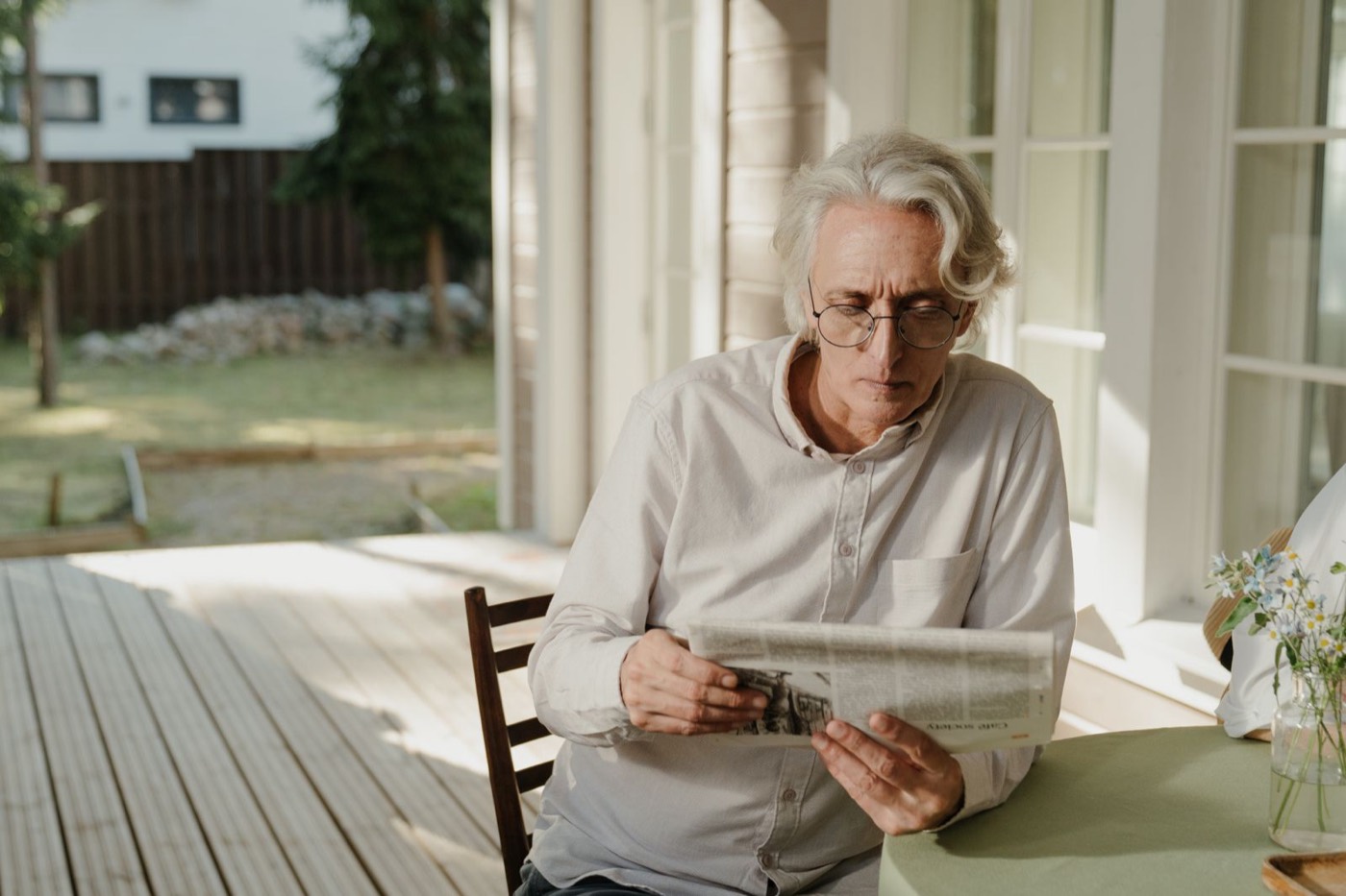 An older man reading on a porch in the morning light